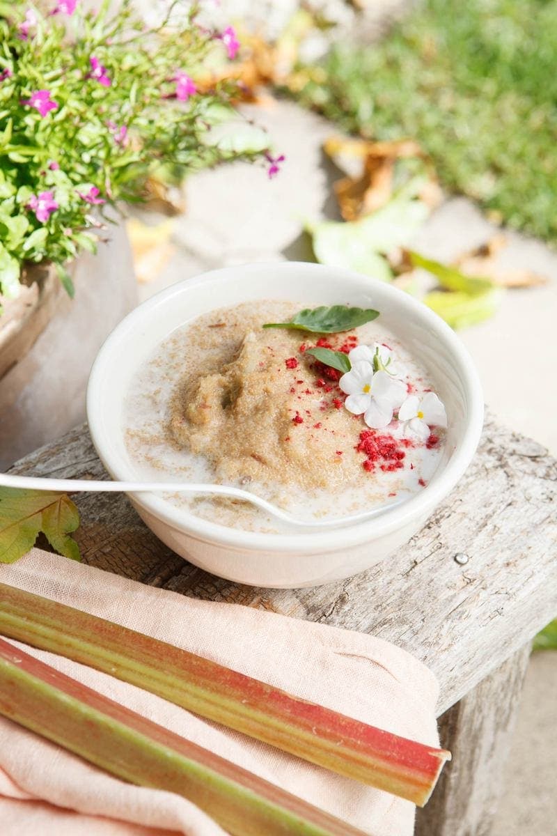 Bowl of Amaranth Porridge on a rustic bench in the garden with rhubarb stalks beside it