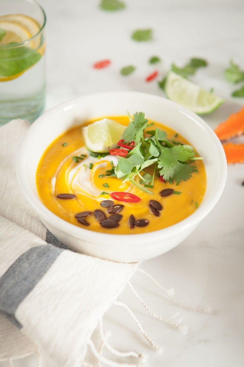 Close up of a bowl of Thai Pumpkin Soup decorated with coconut swirls, chilli, fresh cilantro leaves and lime wedge