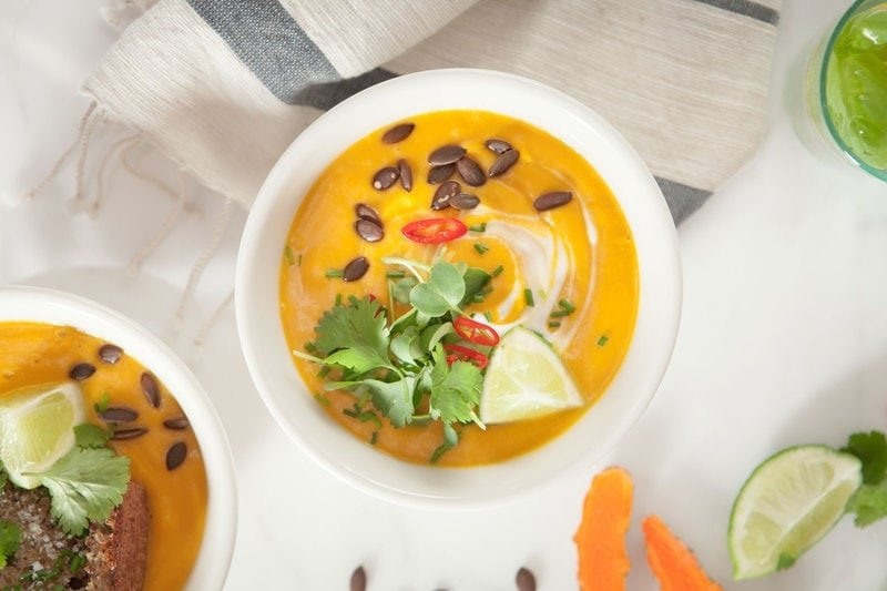 Bowl of bright orange Thai Pumpkin soup with a swirl of coconut yoghurt and toasted pumpkin seeds on top
