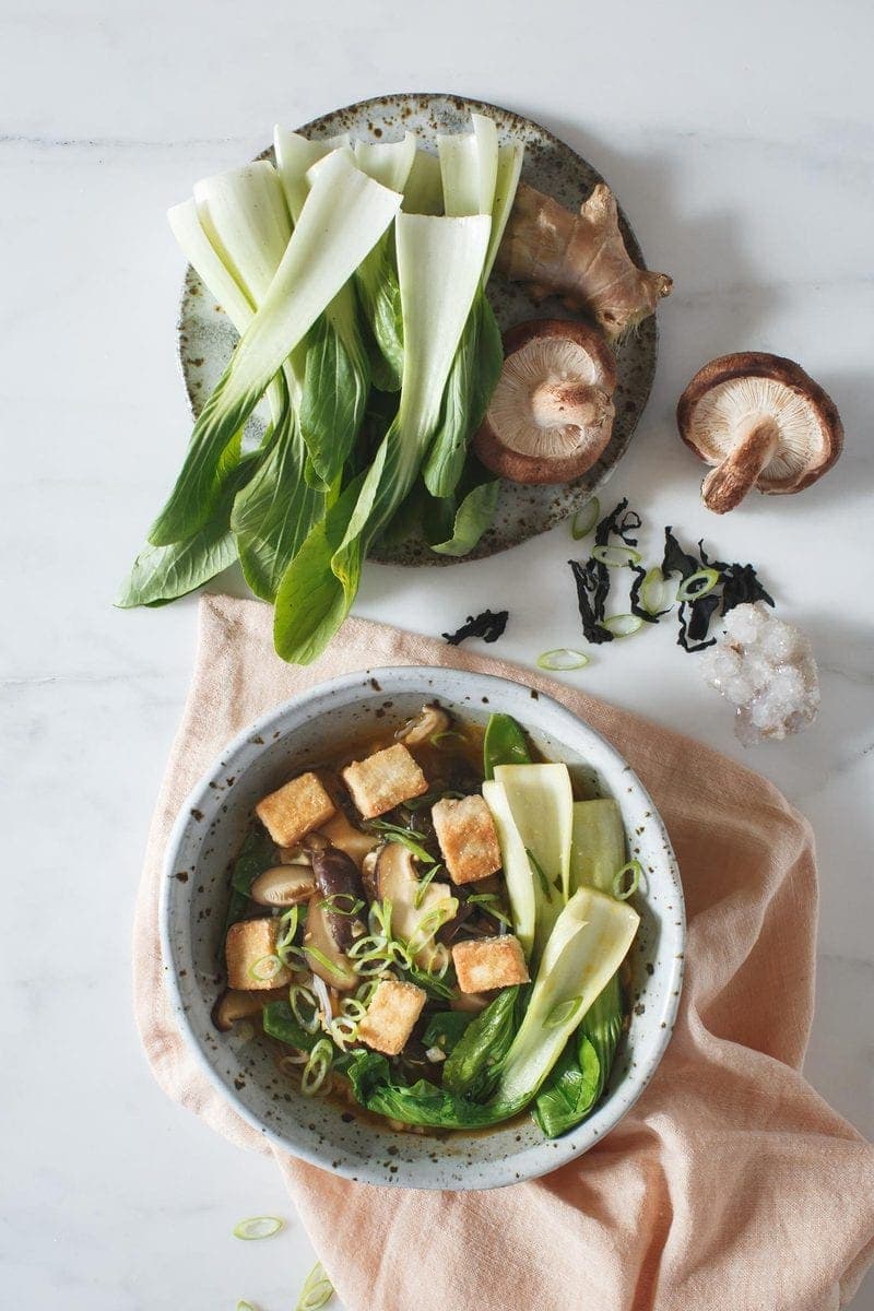 Shiitake Immuno-Soup in a bowl with fresh ingredients on a side plate beside it