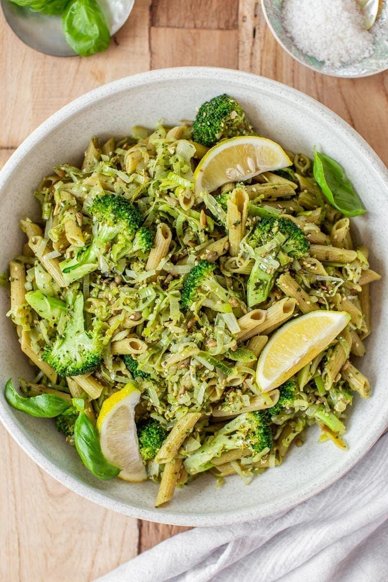 Overhead shot of a large bowl of broccoli pasta tossed with fresh pesto, with lemon wedges on top