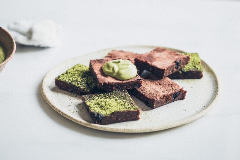 Ceramic plate filled with a stack of raw brownies dusted with matcha