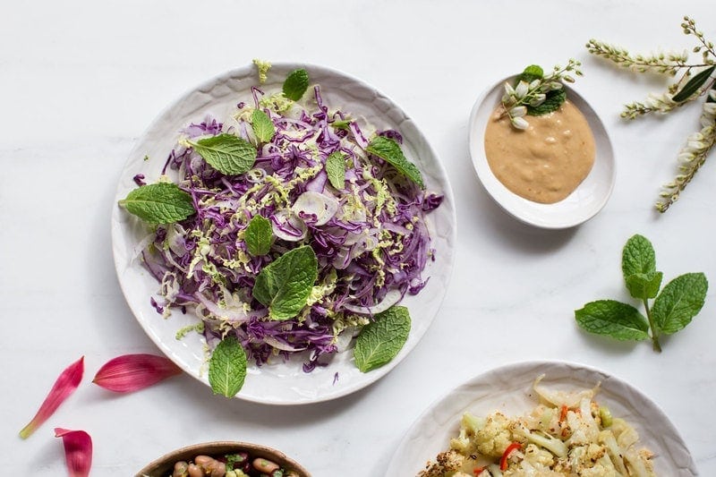Plate of purple coloured slaw and fresh herbs with a tahini dressing on the side