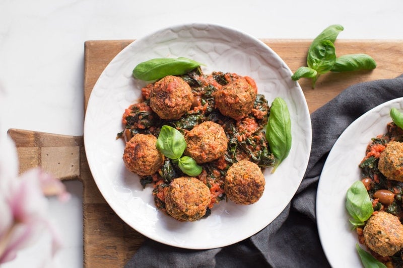 A plate of vegan lentil meatballs in sauce on a chopping board