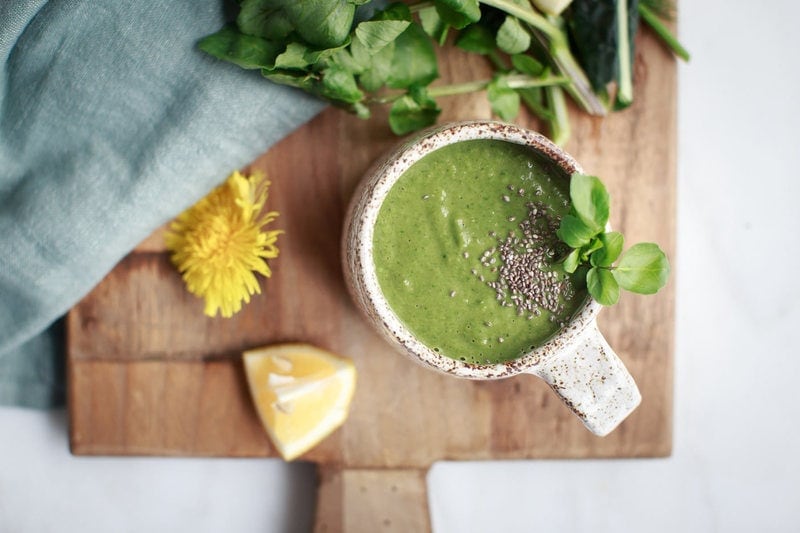 Mug of watercress soup with a few dandelion flowers nearby