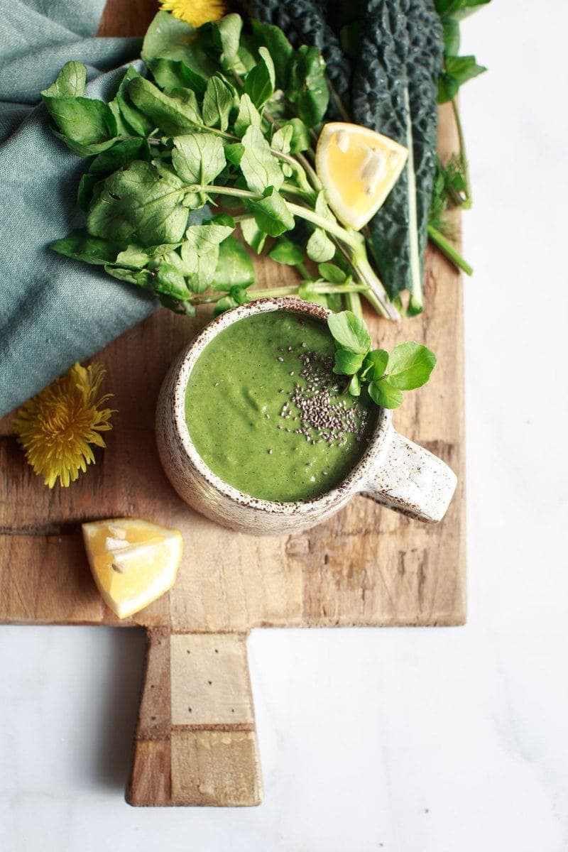 Mug of watercress soup on a wooden board surrounded by fresh ingredients