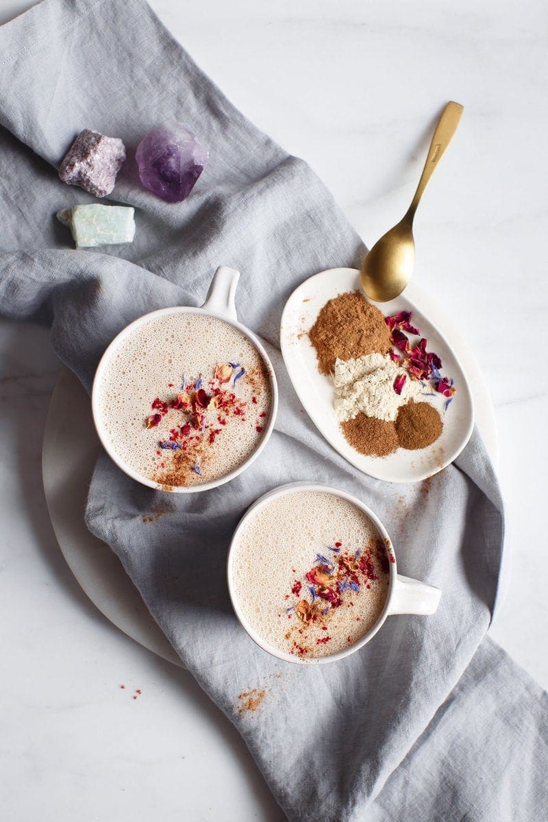 Two ceramic mugs of hot nut milk with ashwagandha and a dish of Ayurvedic spices on a blue linen napkin