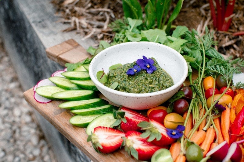 Vegetable platter with pesto on rustic board resting on the edge of a garden bed ready to be enjoyed
