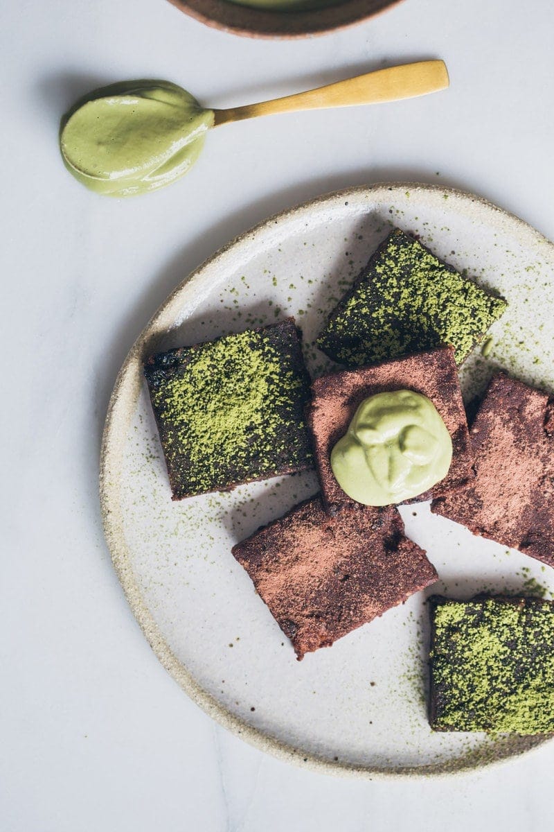Close up of raw vegan brownies on a ceramic plate with a dollop of matcha cream