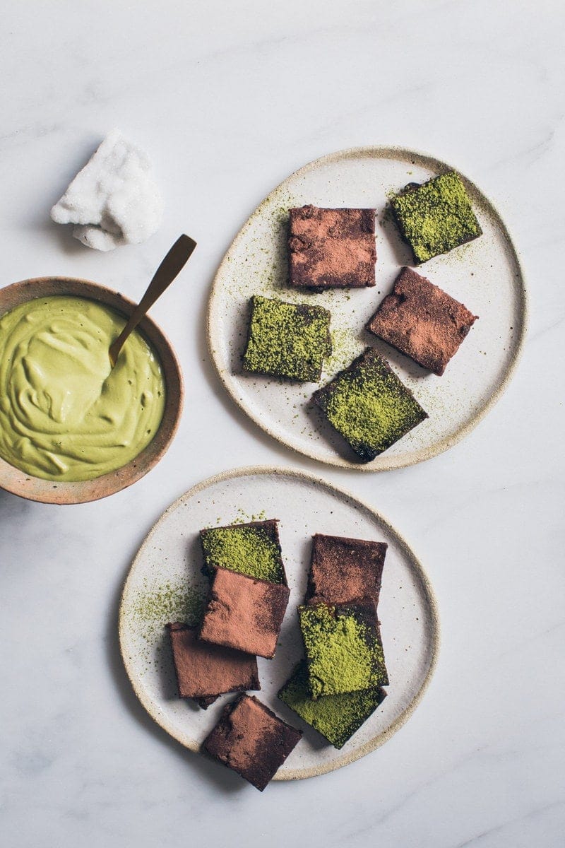 Two ceramic plates filled with vegan brownies and a side bowl of whipped cashew cream