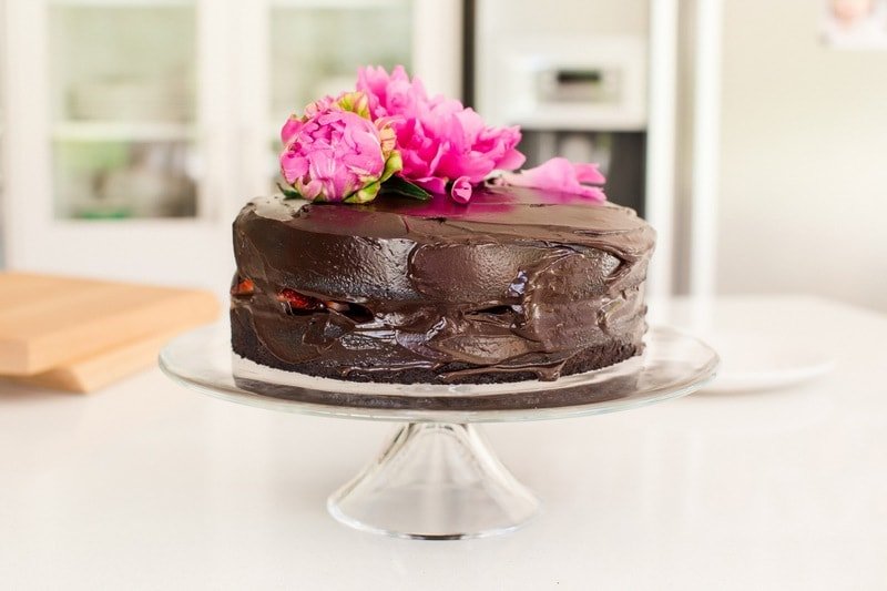 Close up of double layer chocolate cake with strawberries in between, thick coating of chocolate frosting and a pink flower on top