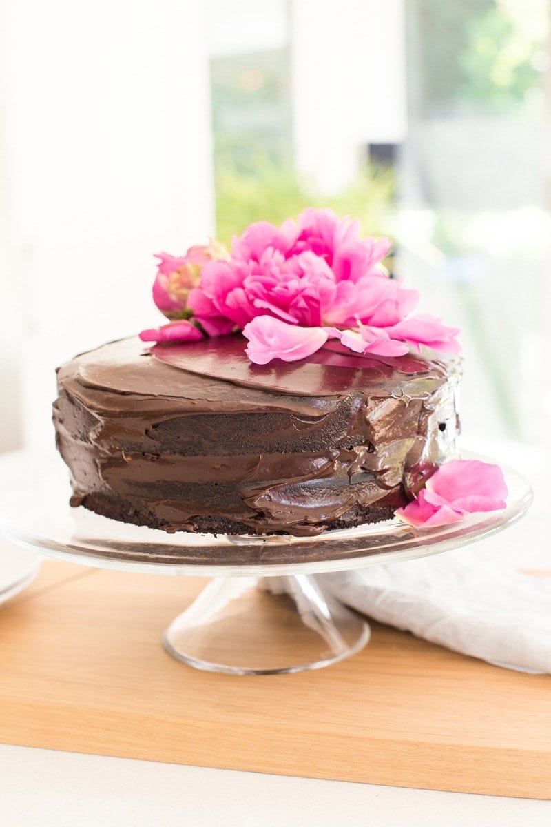 Double layer frosted chocolate cake on a glass cake stand on the kitchen bench