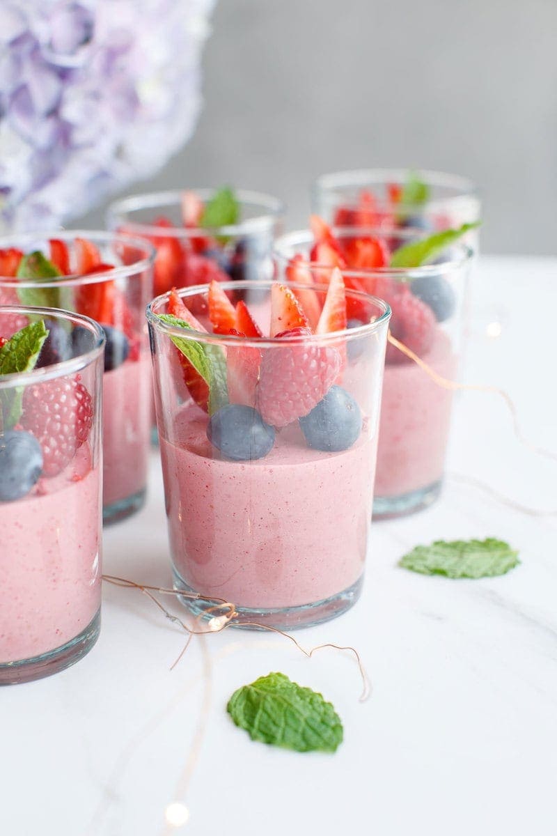 Tea glasses filled with berry mousse with flowers in the background