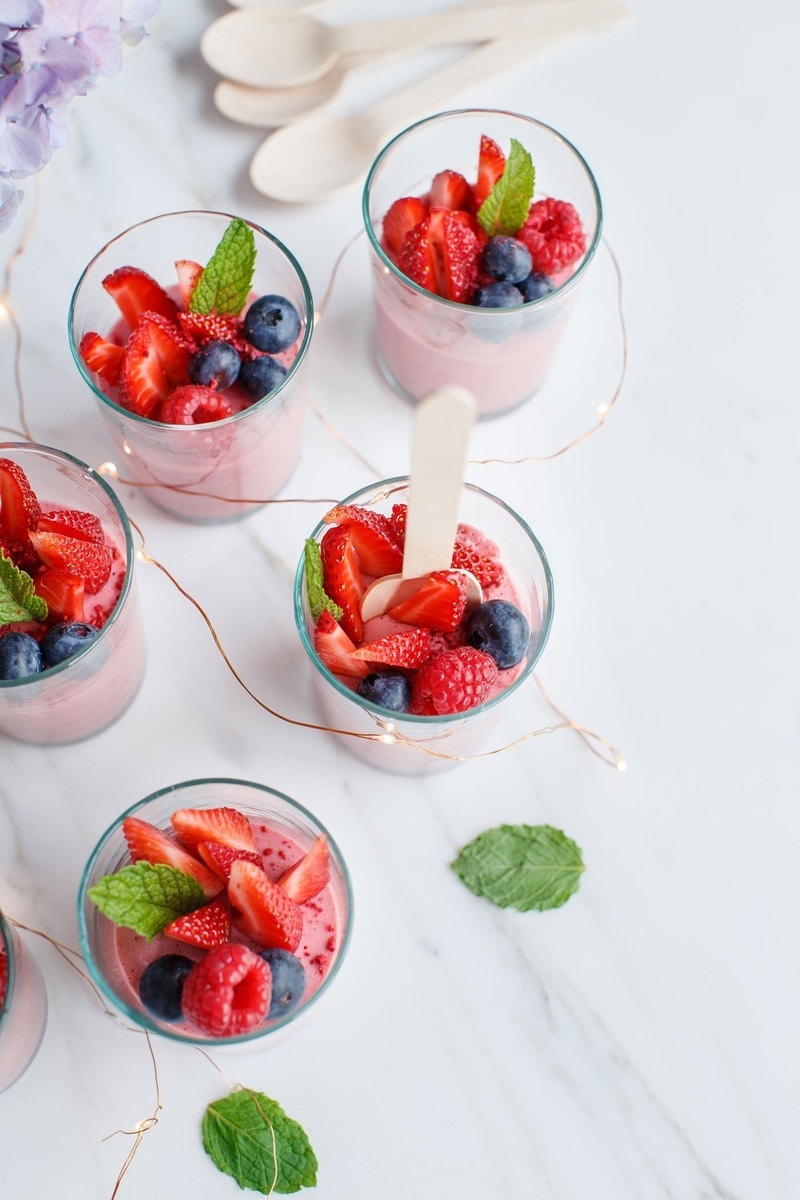 Overhead shot of tea glasses filled with berry mousse with eco spoons resting in cups to serve