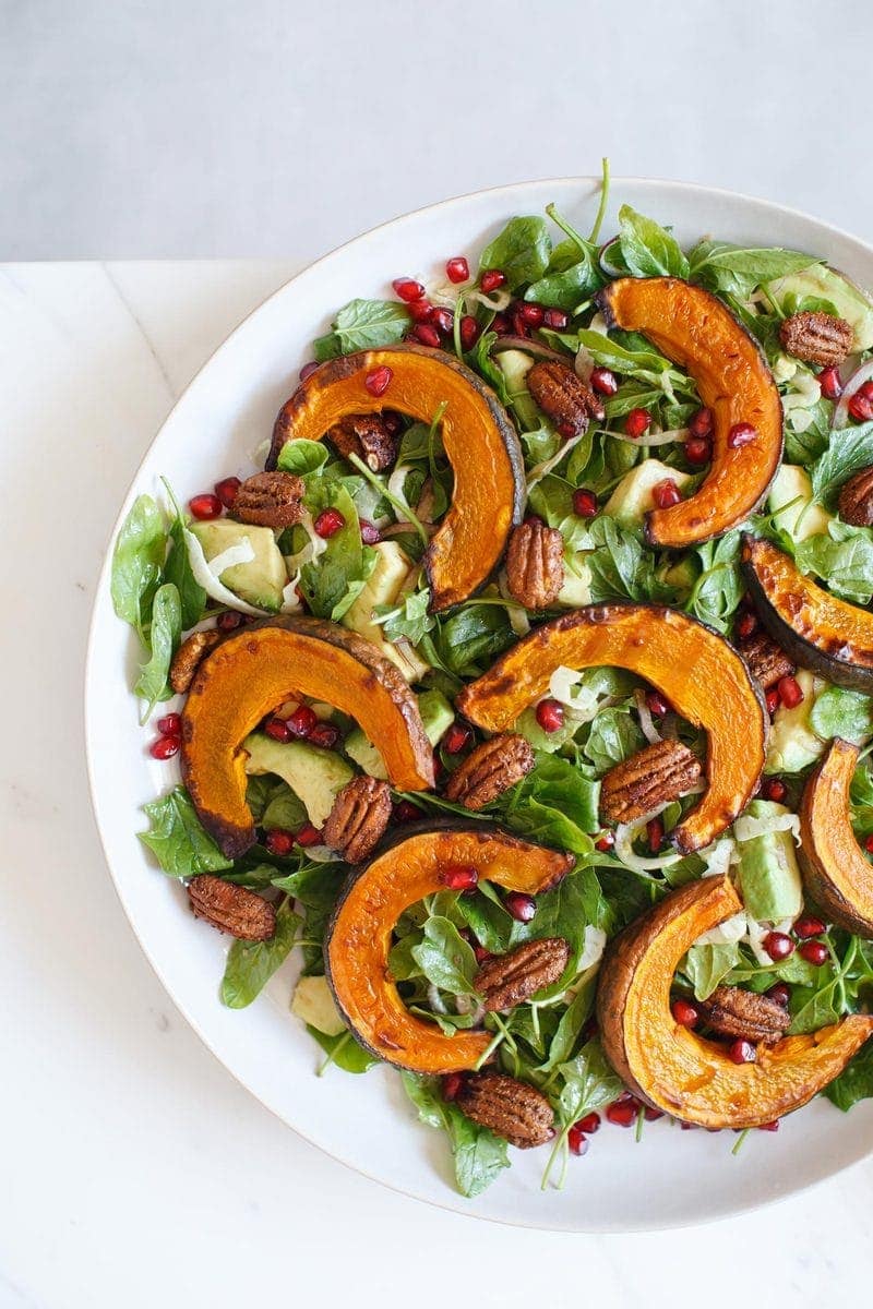 Squash salad with pomegranate and avocado arranged beautifully on a white plate