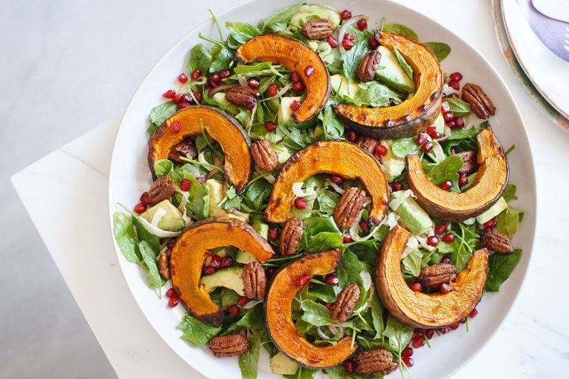 Squash salad next to a stack of coloured ceramic plates