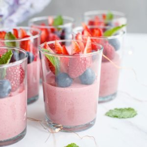 Moroccan tea glasses surrounded by fairy lights, half filled with dairy free strawberry mousse, topped with fresh berries