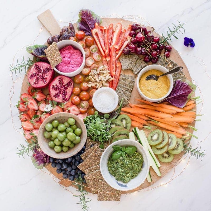Vibrant vegan platter on a wooden board surrounded by fairy lights