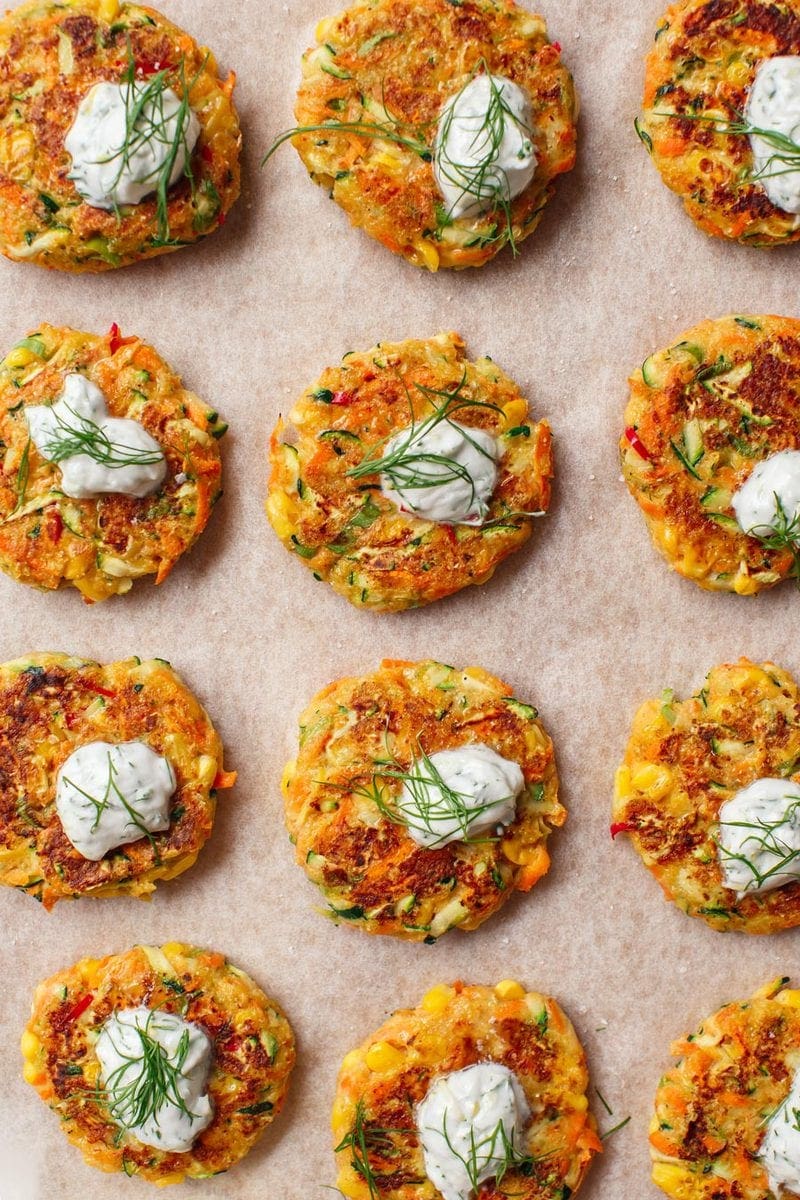 Close up of a dozen bite-sized vegetable fritters on a chopping board garnished and ready to serve