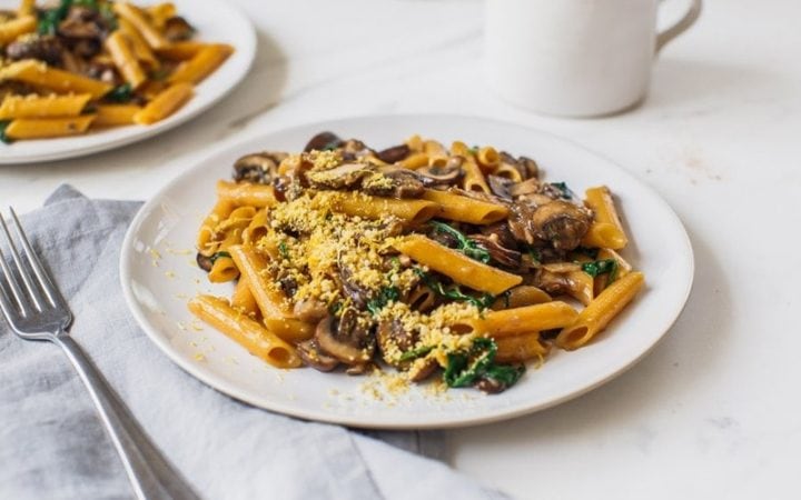 Two plates of creamy mushroom pasta on the kitchen bench with forks and napkins