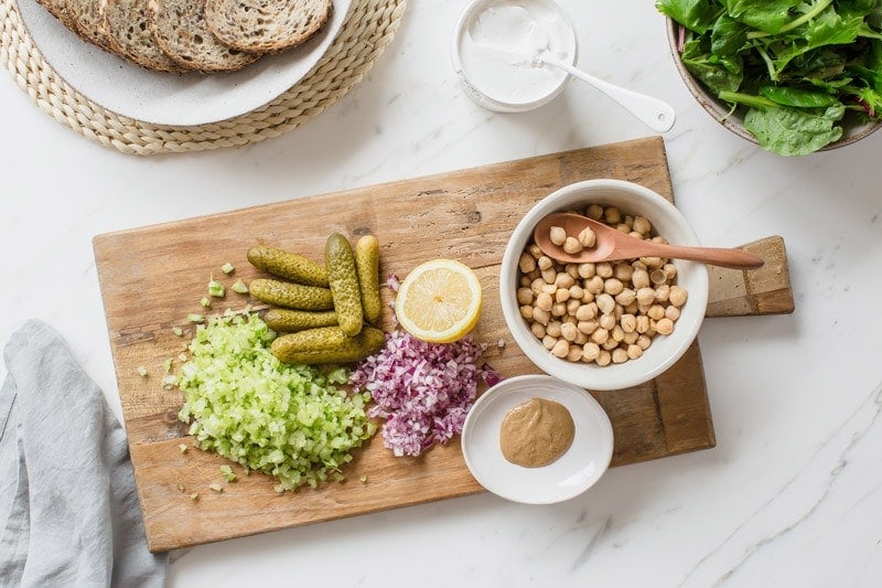 Ingredients for a smashed chickpea salad sandwich filling laid out on a chopping board