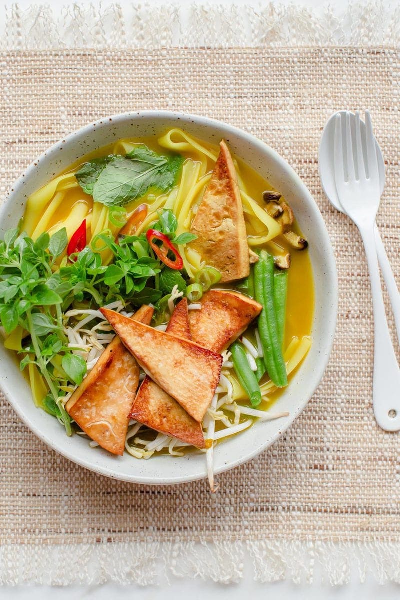 Close up of a delicious bowl of vegetarian pho topped with tofu and shiitake, on a woven placemat