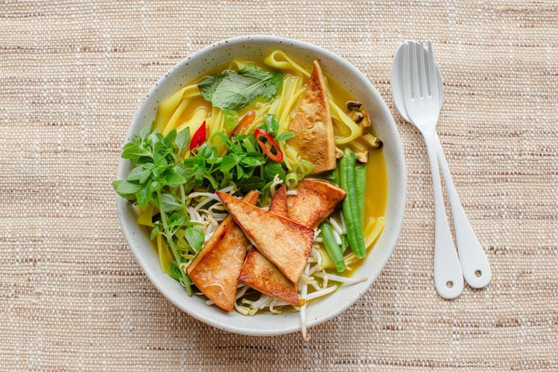 Close up of a bowl of pho made with vegan ingredients, on a woven placemat