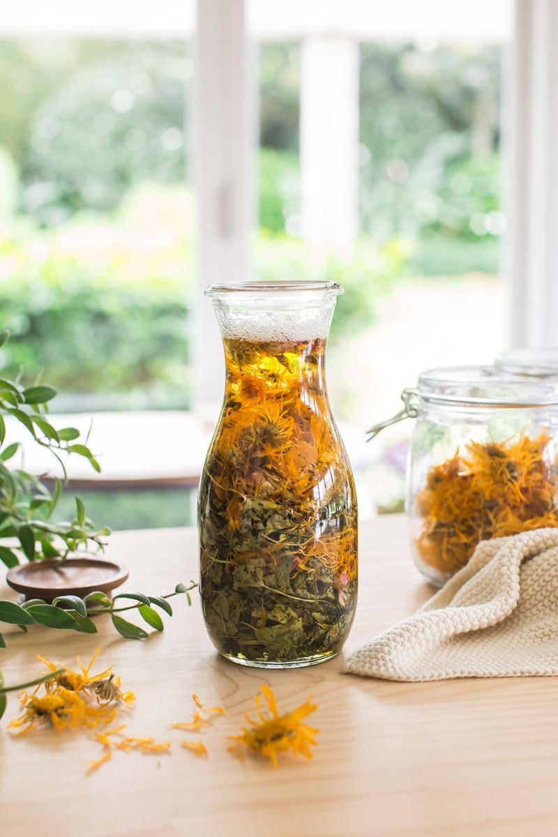 Glass jar filled with herbs and sesame oil for a DIY body oil