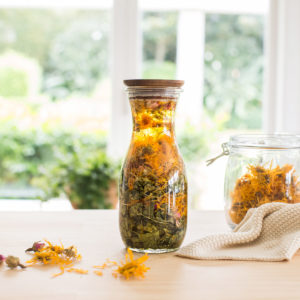 A jar of oil infused with dried herbs on the kitchen counter.