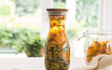 A jar of oil infused with dried herbs on the kitchen counter.