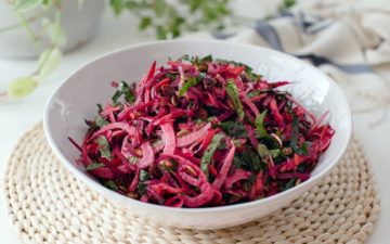 Close up of a bowl of colourful raw beet salad in a white bowl on a woven placemat