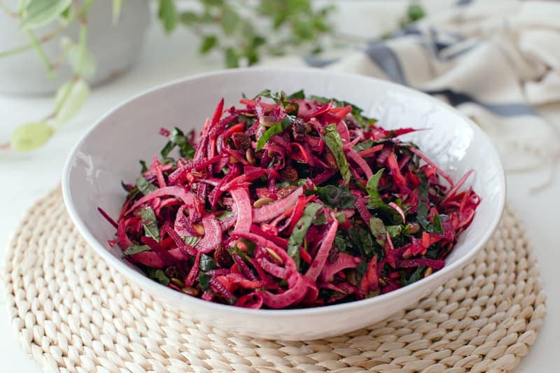 Close up of a bowl of colourful raw beetroot salad in a white bowl on a woven placemat