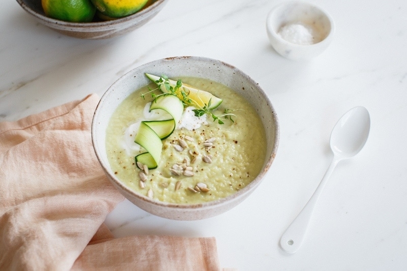 Ceramic bowl of celeriac soup garnished with coconut yoghurt, herbs and lemon on a marble counter