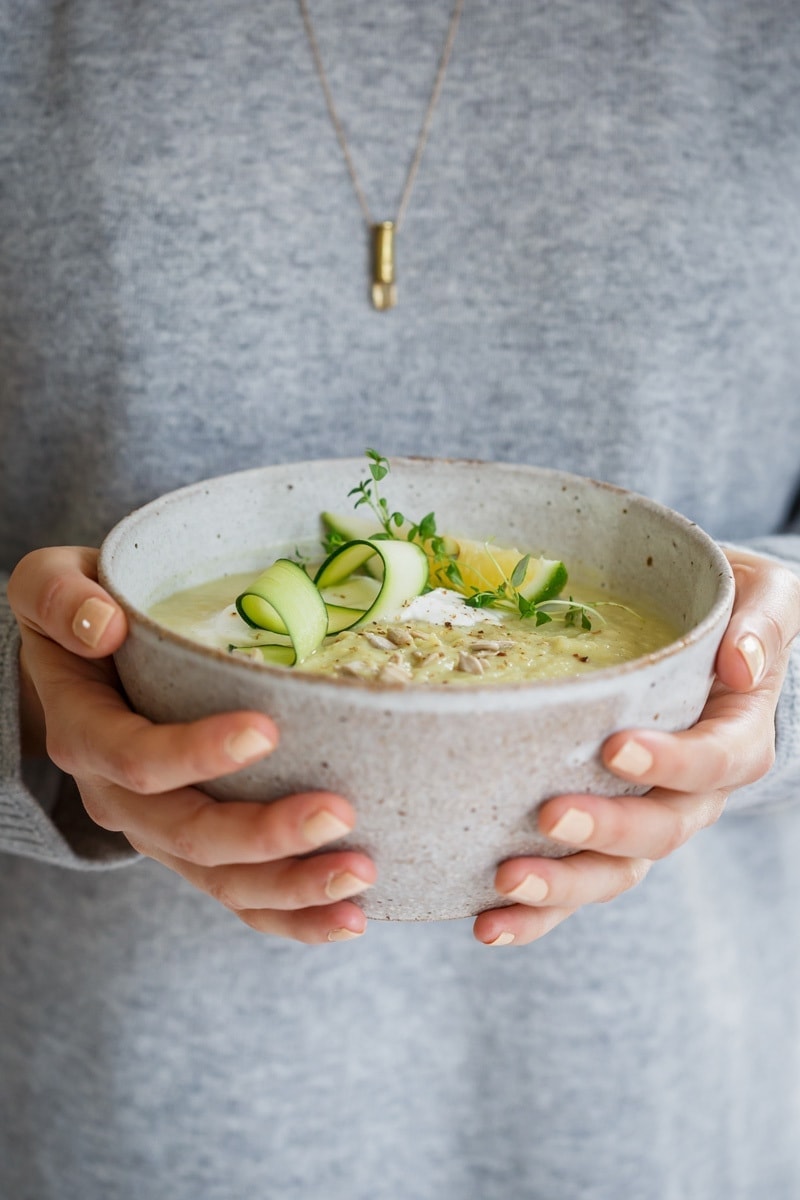 Lauren in a cozy grey sweater holding a ceramic bowl of homemade celeriac soup with beautiful garnishes