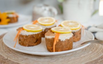 A plate of four individual raw carrot cake muffins topped with lemon cashew frosting on a woven placement