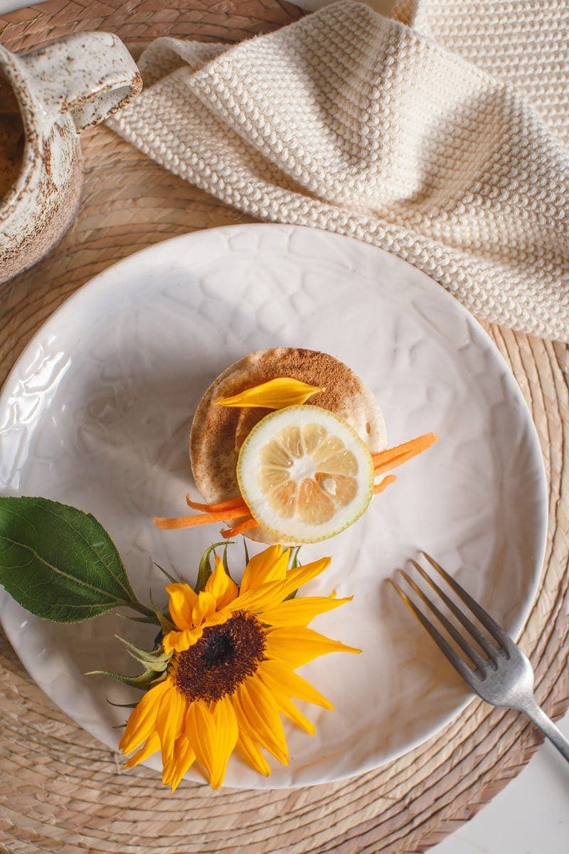 A mini raw carrot cake on a plate with a sunflower beside it