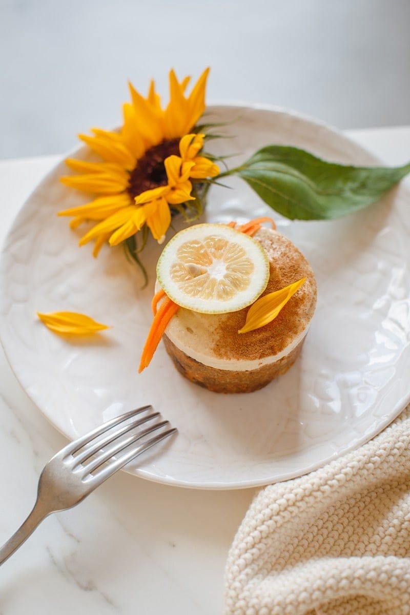 A mini raw carrot cake with lemon frosting on a plate on a marble surface