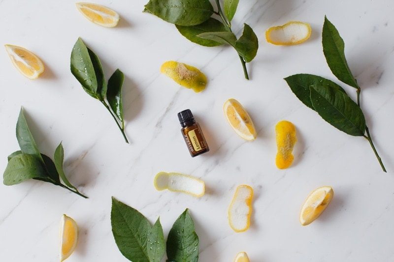 doTERRA lemon essential oil surrounded by fresh citrus peel and leaves on a marble surface