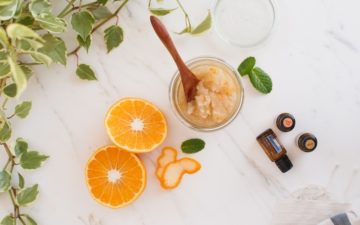 A homemade sugar scrub on the bench with grapefruit, ginger and peppermint essential oil bottles