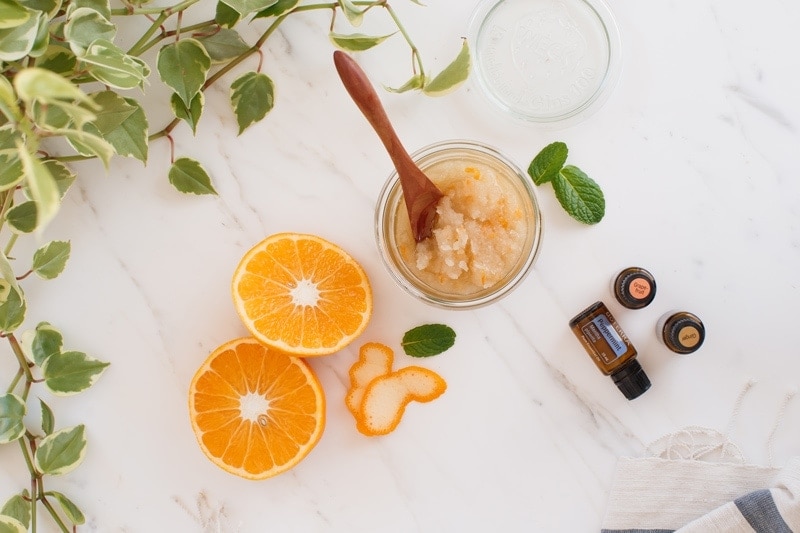 A homemade sugar scrub on the bench with grapefruit, ginger and peppermint essential oil bottles