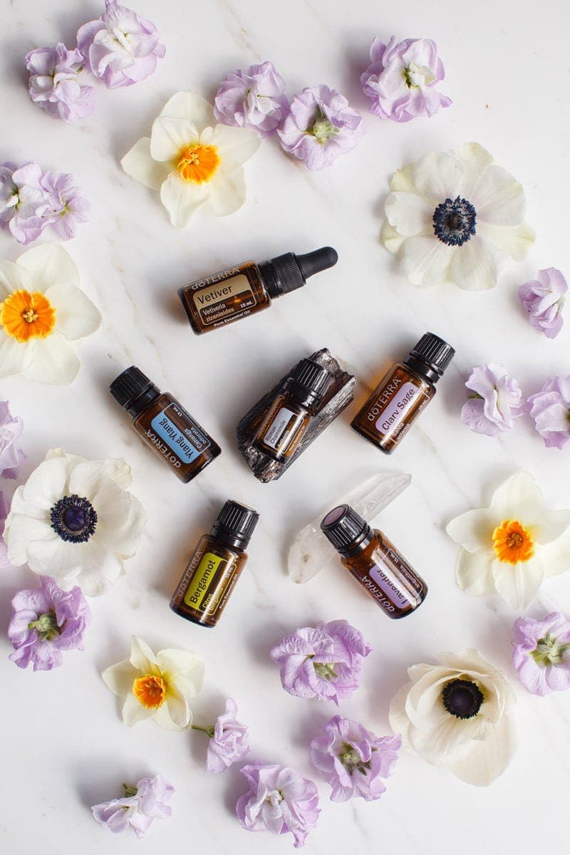 6 essential oils for stress on a marble surface surrounded by colourful flowers