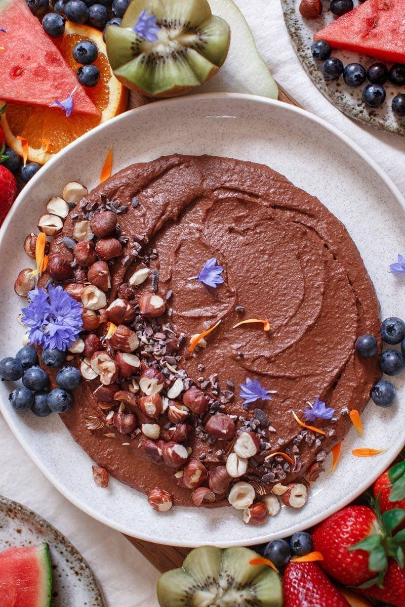 Close up of a bowl of chocolate hummus with cacao nibs and roasted nuts on top
