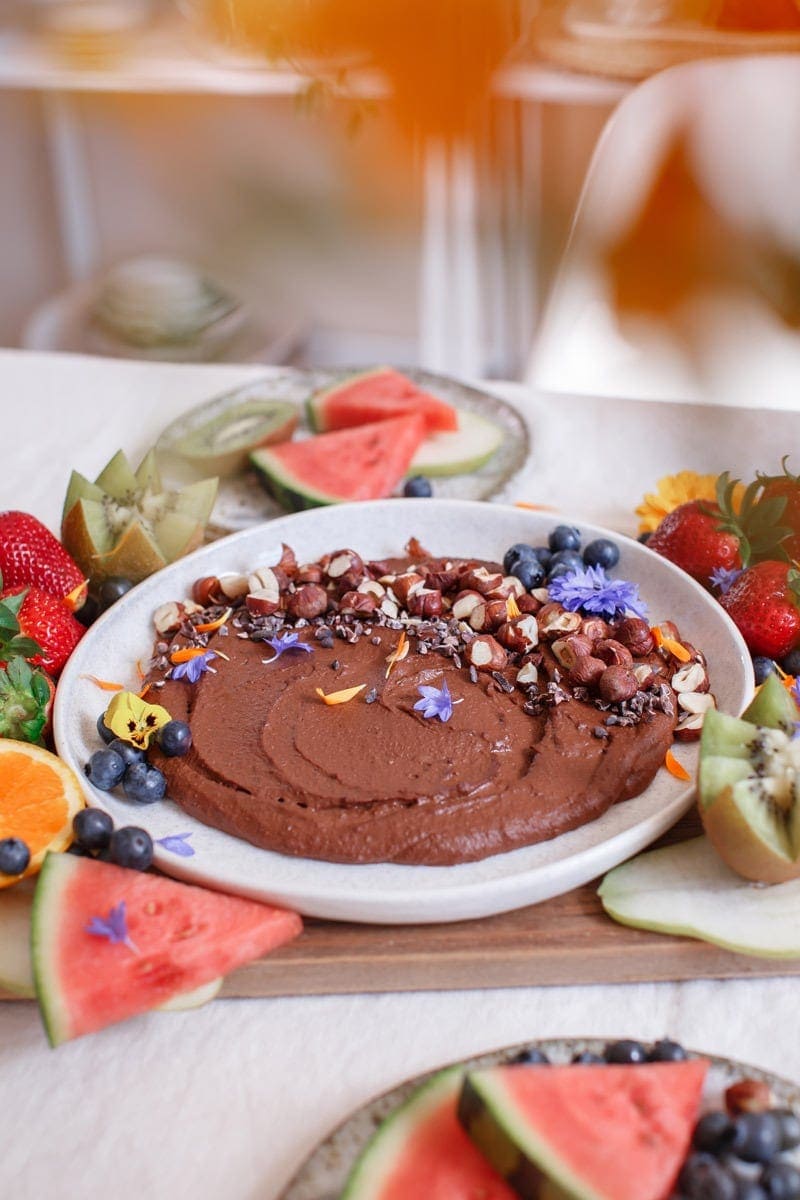 Bowl of chocolate hummus on the dining table surrounded by fresh fruits ready to enjoy