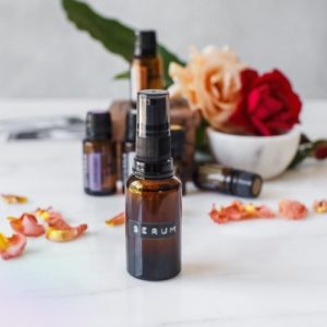 Bottle of serum surrounded by essential oils and rose petals on a bathroom counter