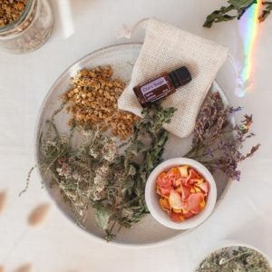 Ceramic plate filled with dried herbs, flower petals and a bottle of clary sage oil, all are ingredients needed to make a herbal bath