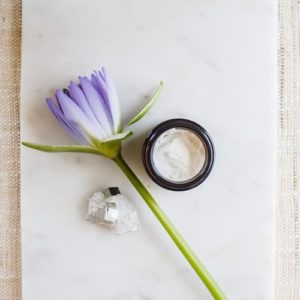 Pottle of skin cream on marble, with a water lily beside it.