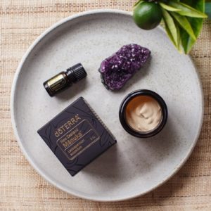 Small amber jar filled with homemade face cream styled beautifully on a plate with a crystal and some fresh flowers.