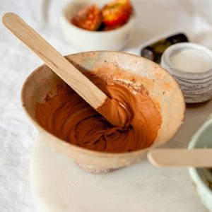 Earthy red clay mask in a ceramic dish.