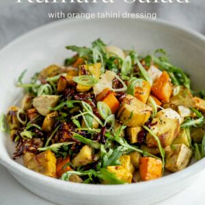 Bowl of roast kumara salad topped with sliced spring onions. Text over the top reads "Kumara salad with orange tahini dressing".