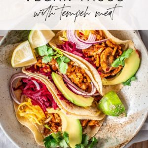 Hero shot of the colourful tempeh tacos squished together on a plate, with the recipe title at the top.